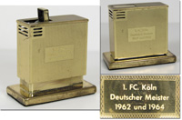 Hochwertiges, dekoratives Tischfeuerzeug mit der Inschrift "1.FC Kln Deutscher Meister1962 und 1964". Vergoldet, Gasbertieb, 7,5x4x6,5 cm.<br>-- Schtzpreis: 100,00  --