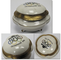 Porzellandose mit Deckel. Deckel mit farbigen Olympischen Ringen und Inschrift Olympiade 1936. Hhe: 7,5 cm. Durchmesser: 11 cm.