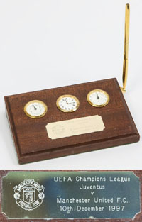 Tischwetterstation mi Thermometer, Hydrometer und Quartzuhr auf Holzsockel mit Kugelschreiber. Aufmontiert gravierte versilberte Plakette mit dem Logo von Manchester United und der Aufschrift "UEFA Champions League Juventus - Manchester United FC. 10th Dec