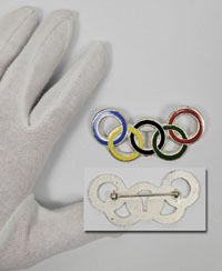 Groe Anstecknadel mit farbig emaillierten Olympischen Ringen. Bronze versilbert, 7,5x3,8 cm.<br>-- Schtzpreis: 75,00  --